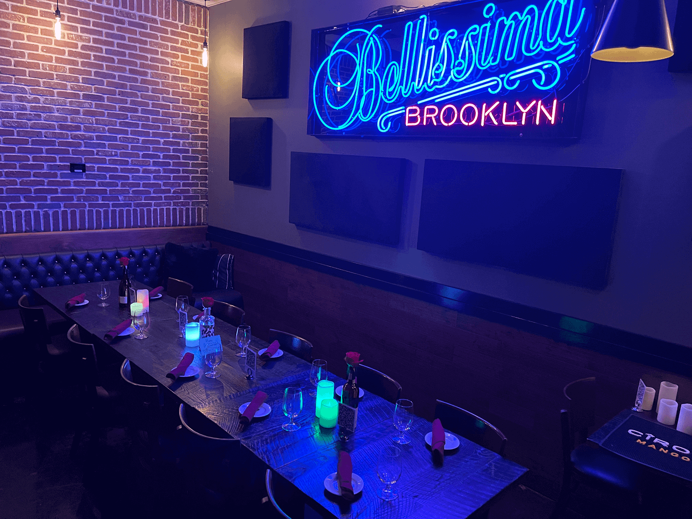 Interior of Brooklyn Trattoria's event space. A long table with bench seating under a neon sign that reads 'Bellissima Brooklyn'